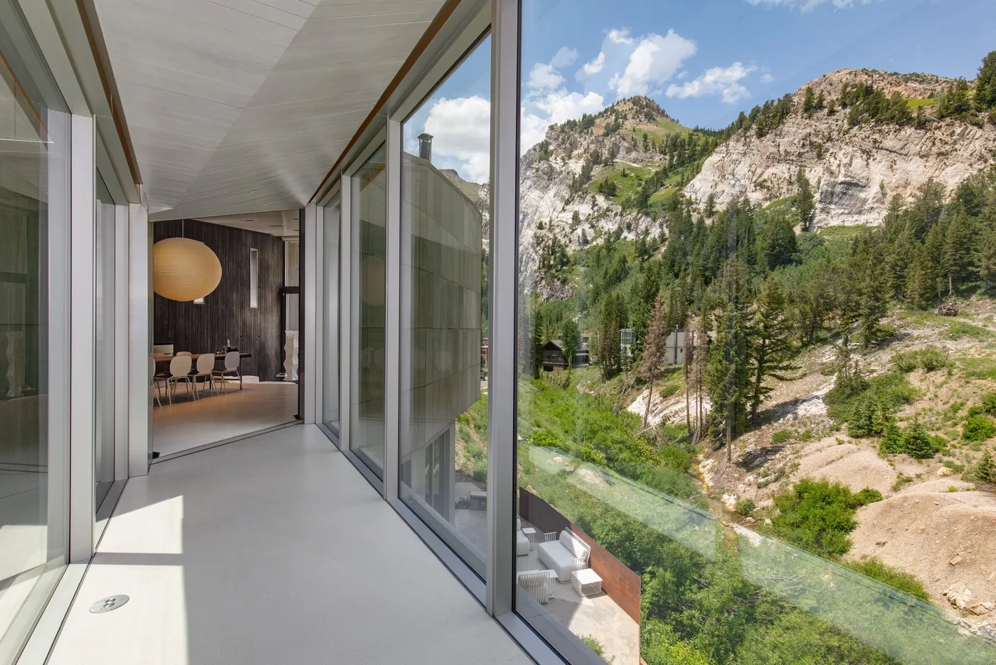 A glass-walled balcony overlooks a forested mountain landscape.