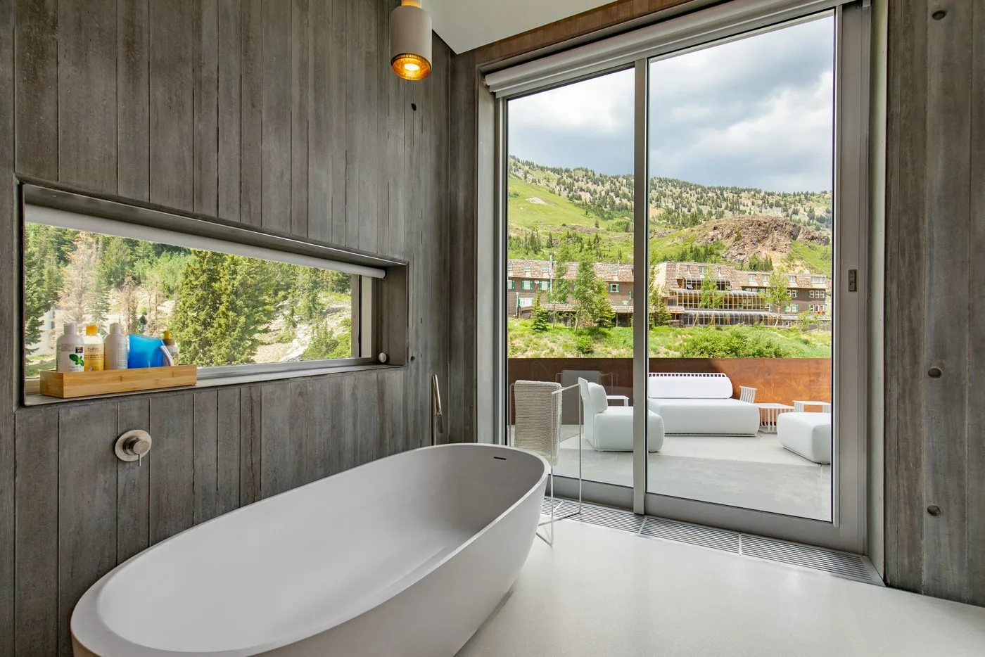 A bathroom with a freestanding bathtub beside large windows overlooking green hills.