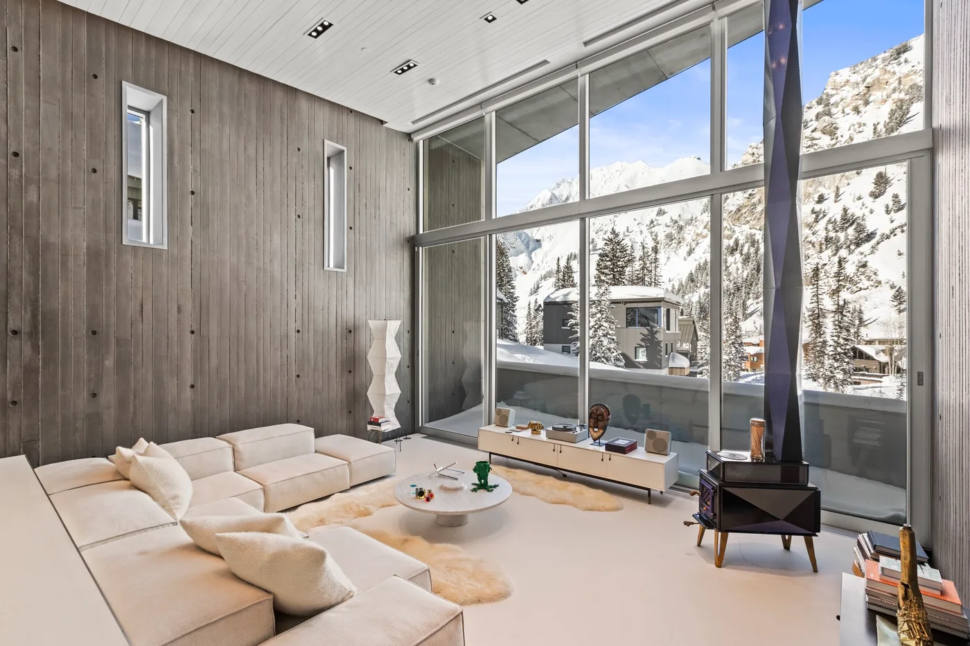 A modern living room with light seating and large windows overlooking a snowy mountain landscape.