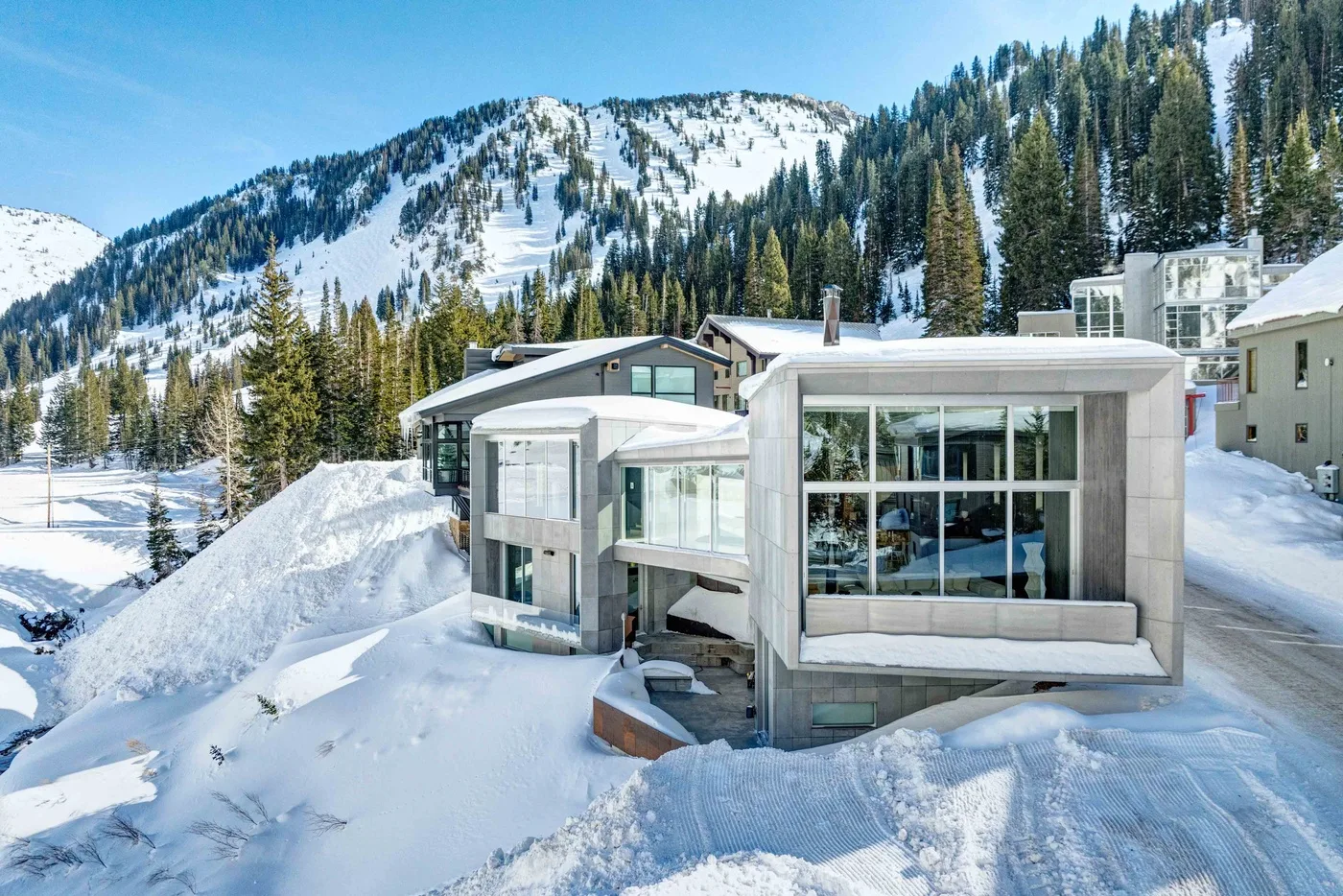 A modern building sits amid deep snow, with a forested mountain rising behind it.