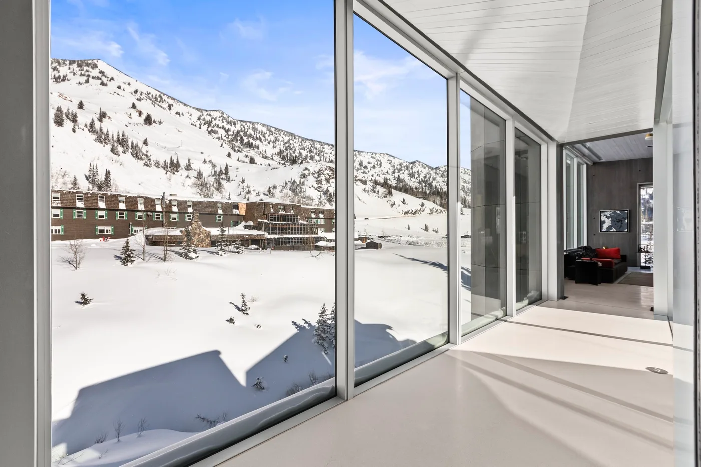 A bright glass-walled room overlooks a snow-covered mountain and nearby buildings.
