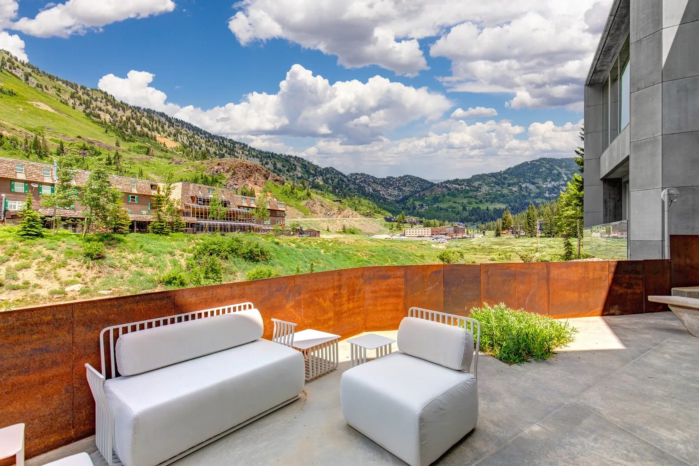 An outdoor patio with cushioned seating overlooks a green mountain valley.