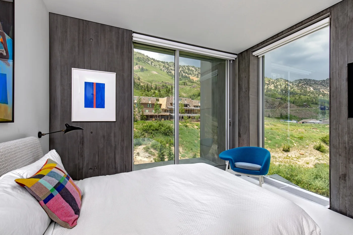 A bedroom with a bed and large windows overlooking green hills.