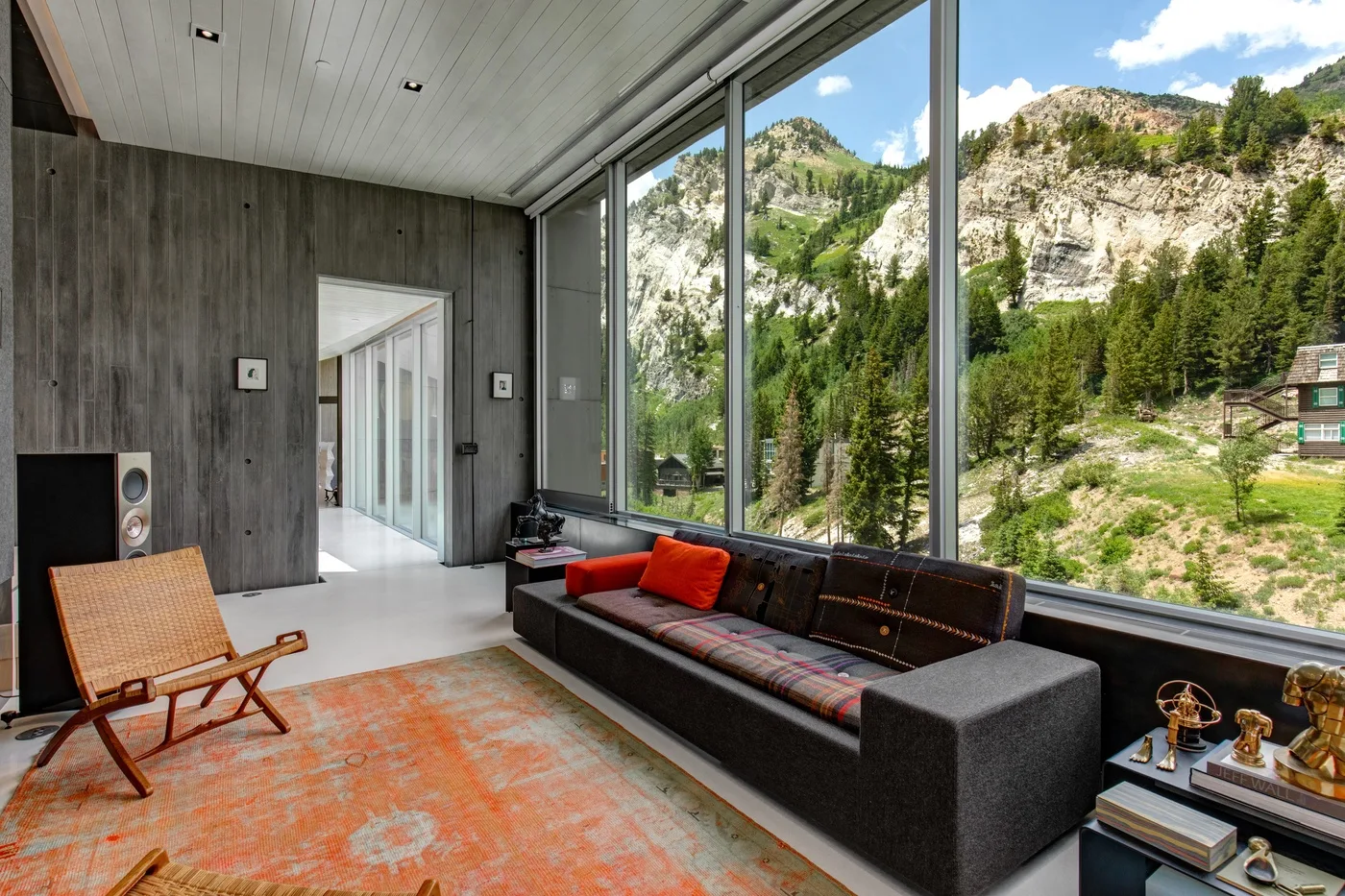 A modern living room with a dark sofa and floor-to-ceiling windows overlooking a mountain landscape.