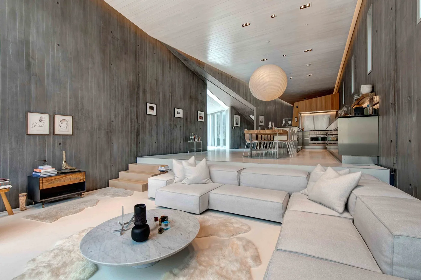 A modern living room with sectional seating opens onto a dining area and kitchen.