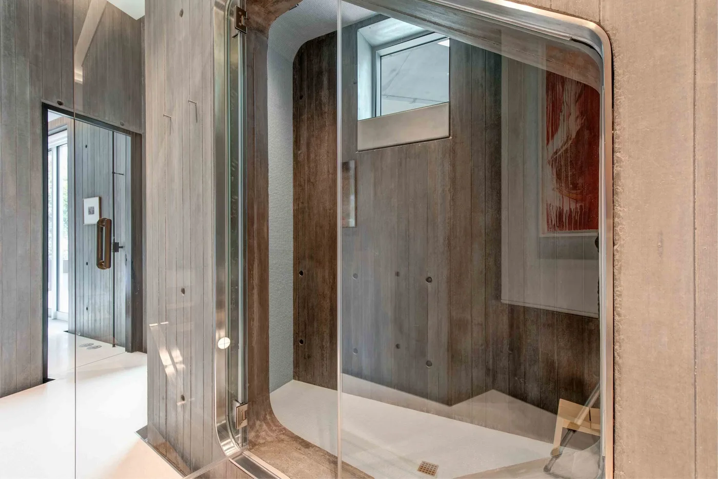 A glass-enclosed shower sits beside a wood-paneled bathroom wall.