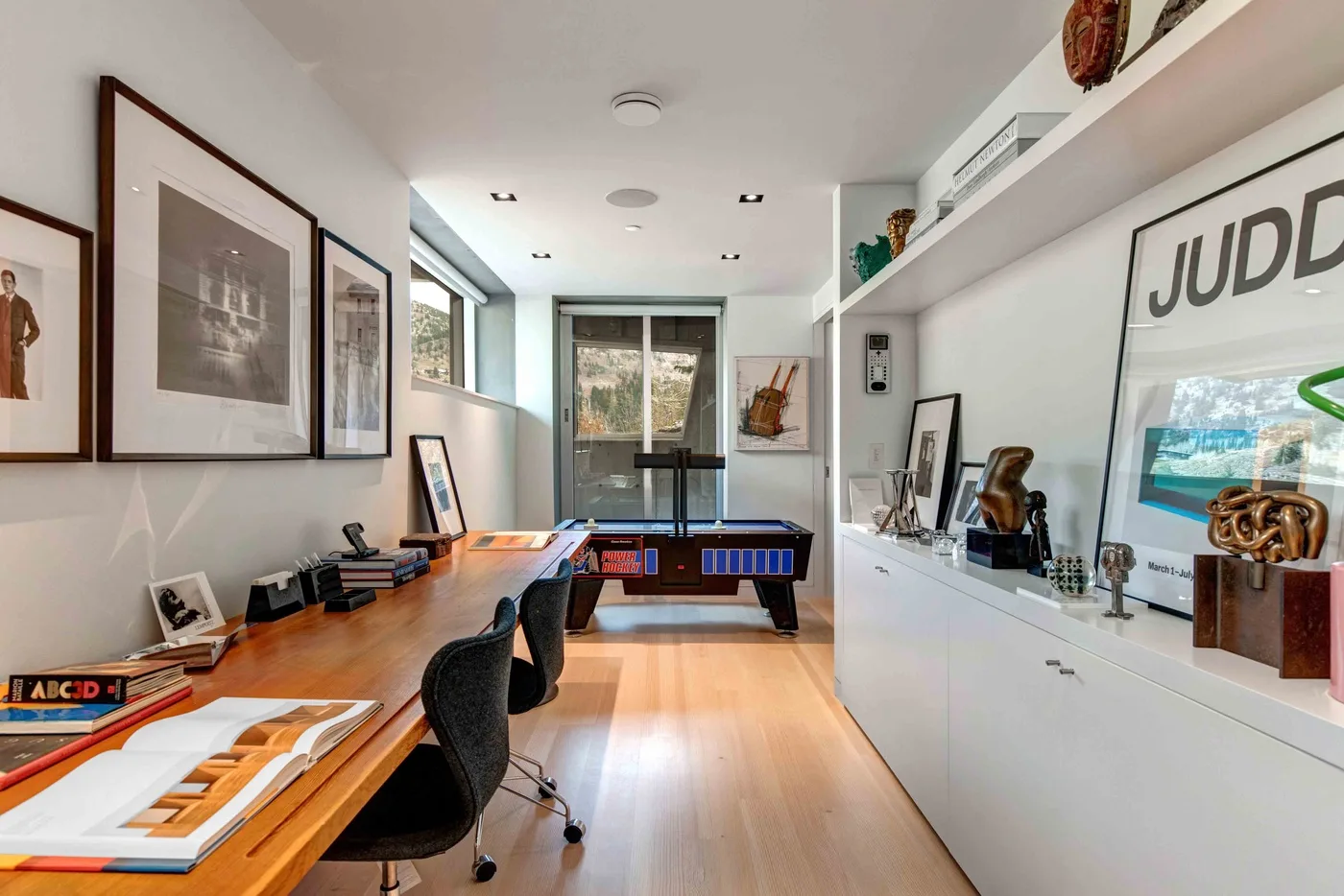 A bright home office with a long desk and a pool table.