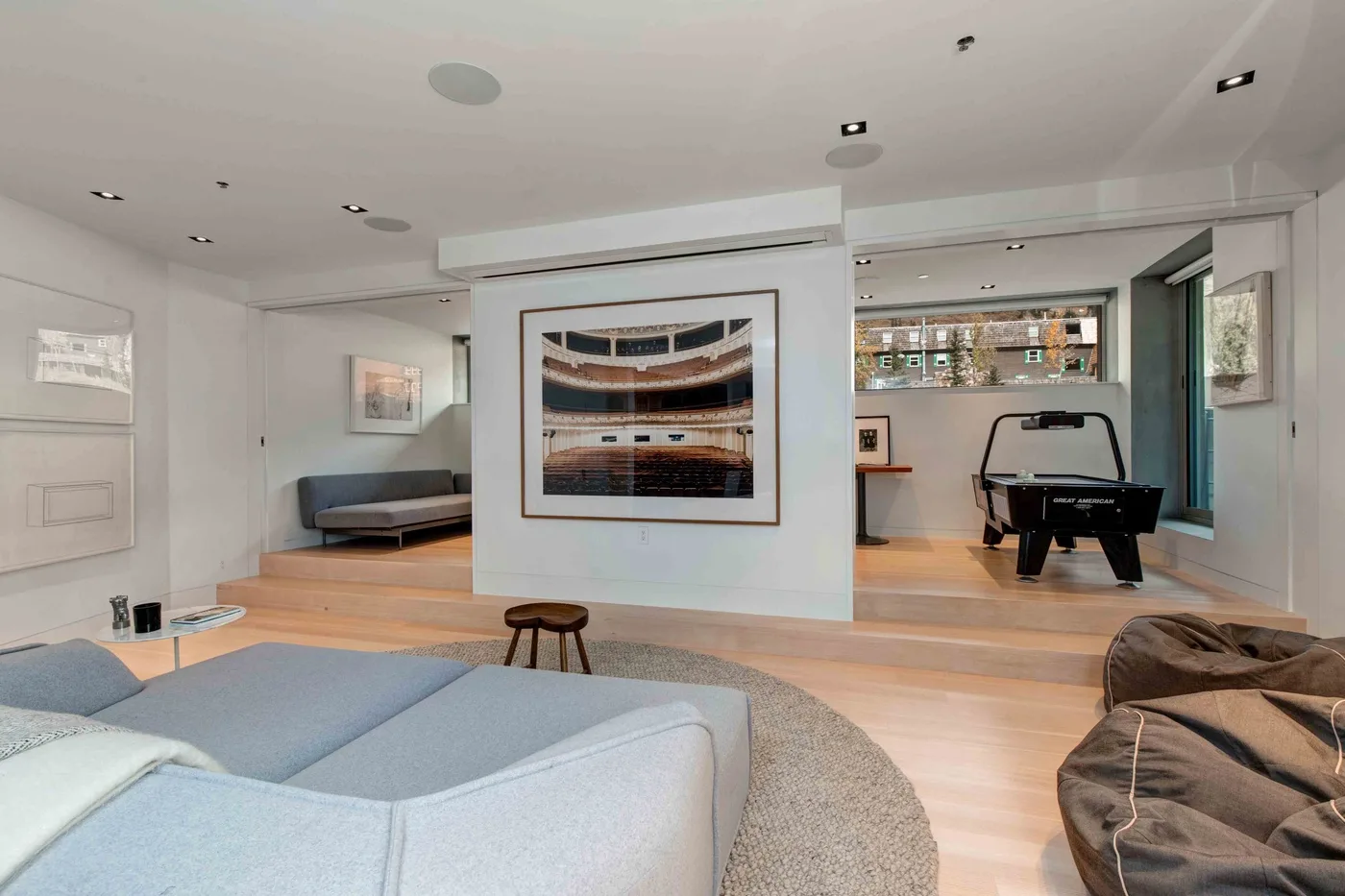 A modern living room with seating, framed artwork, and a pool table in the adjoining space.