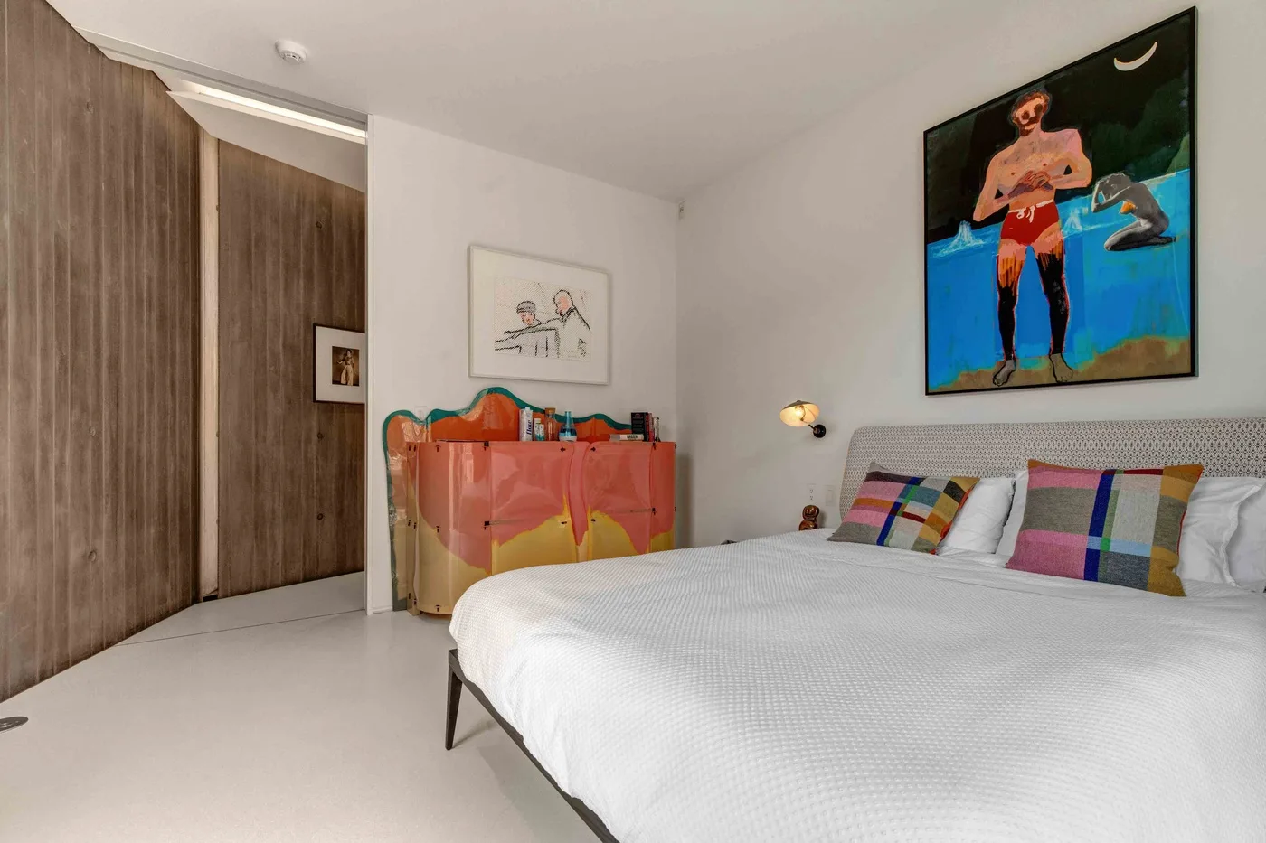 A bedroom with a bed, colorful headboard, and artwork on the walls.