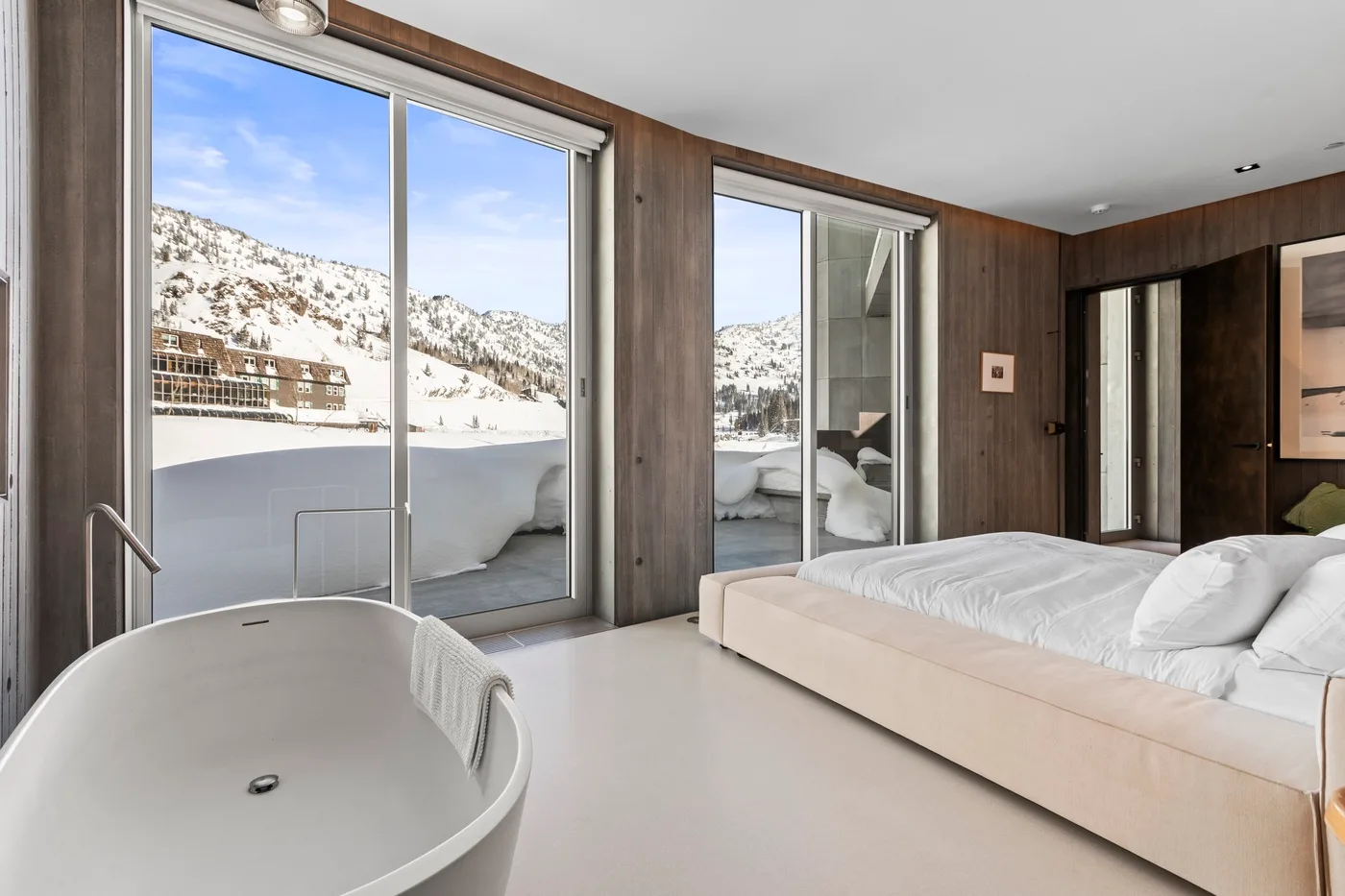 A bedroom opens onto a snowy mountain view through large glass doors.