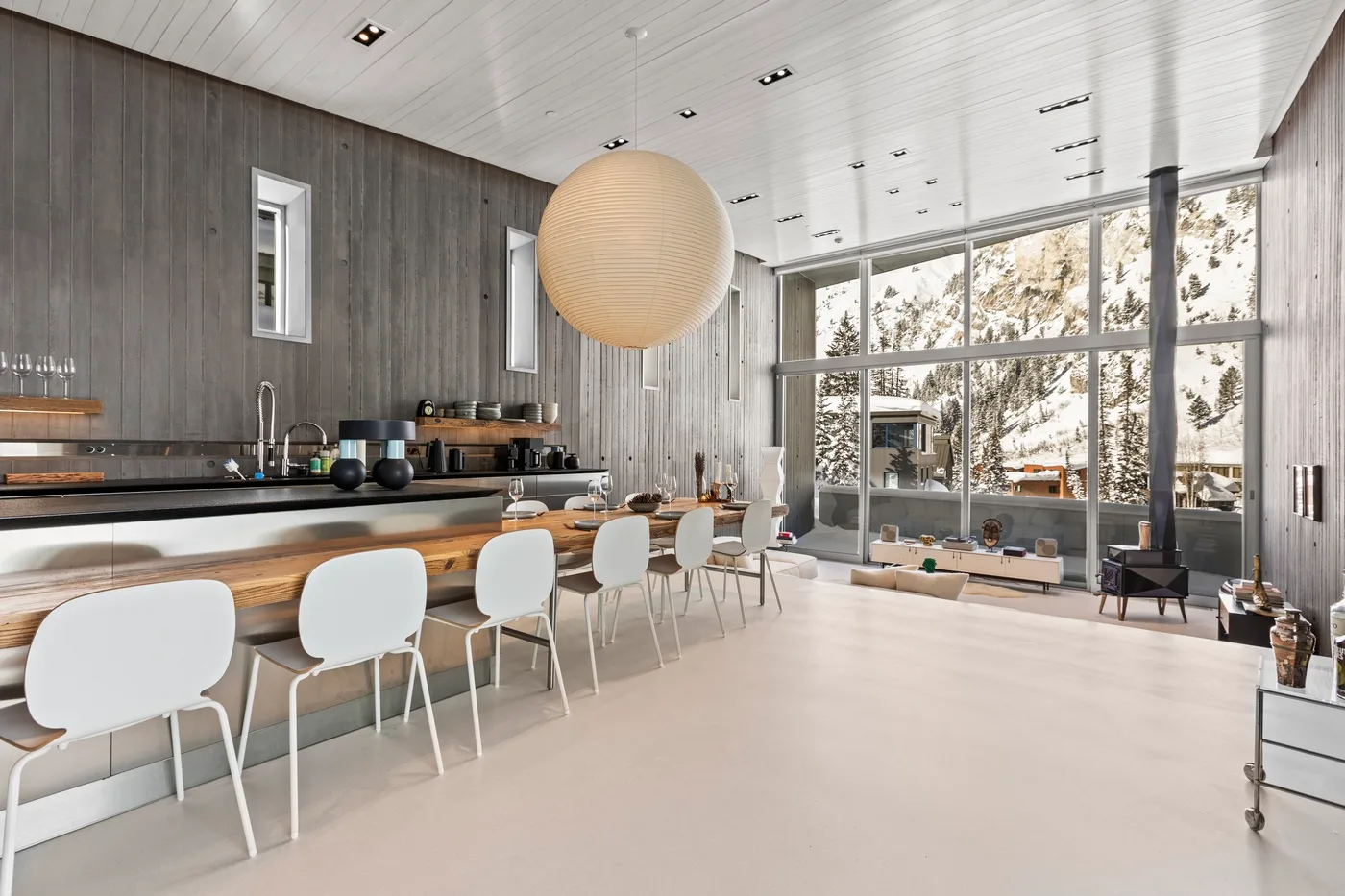 A modern kitchen and dining area opens onto large windows overlooking the outdoors.