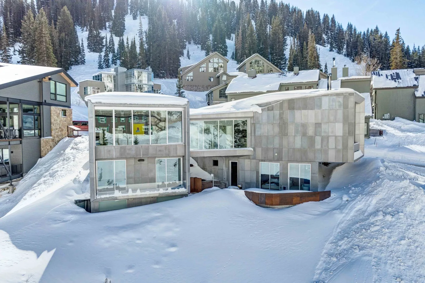 A modern building sits in a snowy mountain setting among evergreen trees.
