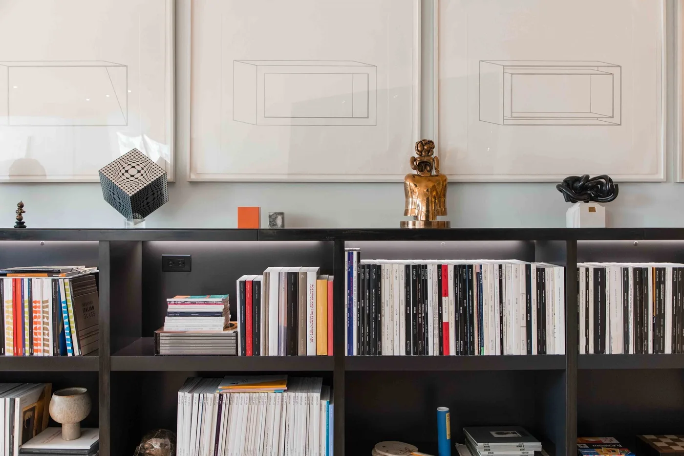 A dark bookshelf filled with books and records stands beneath framed artwork.