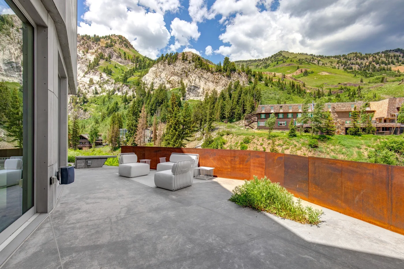 A spacious outdoor terrace with seating overlooks green hills and trees.