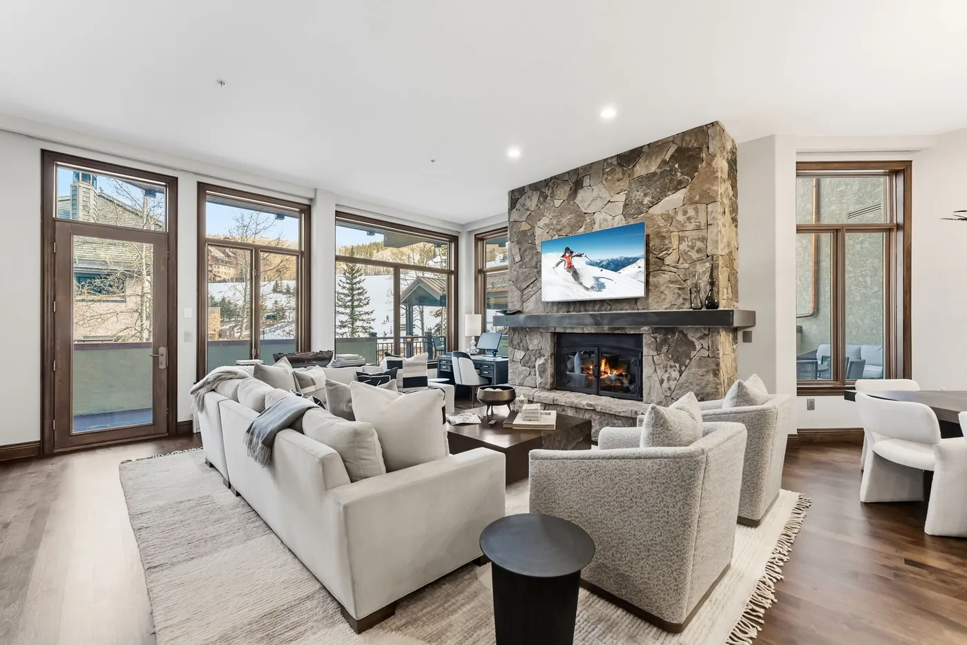 A living room with seating arranged around a stone fireplace and large windows.