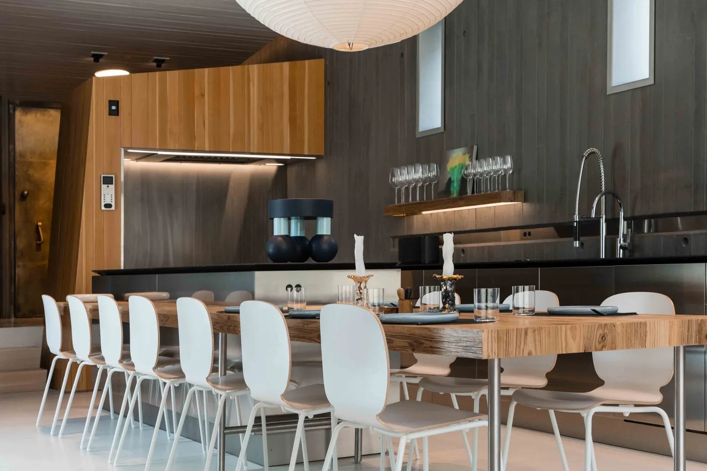 A dining area with a long table and white chairs beside a kitchen counter.