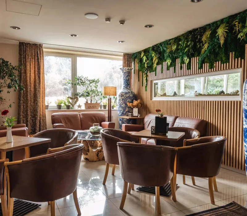 Zona de estar del vestíbulo con sillones de cuero, grandes ventanales y detalles de madera.
