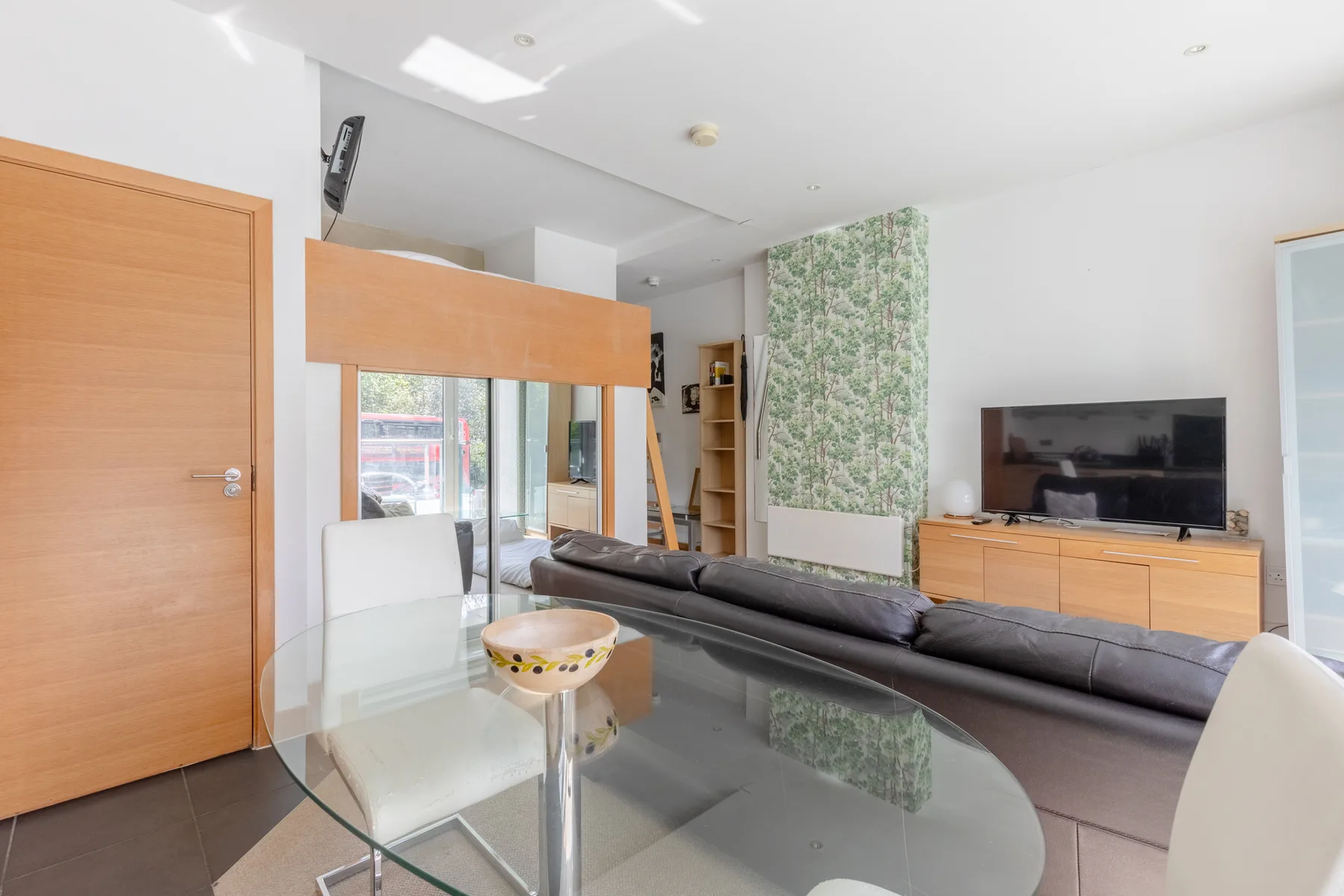 A bright living room with a glass dining table and television.