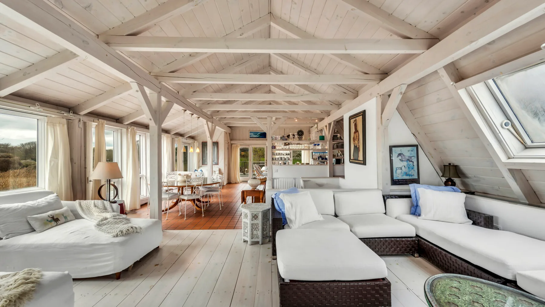 A bright open-plan living and dining area with white seating and exposed timber beams.