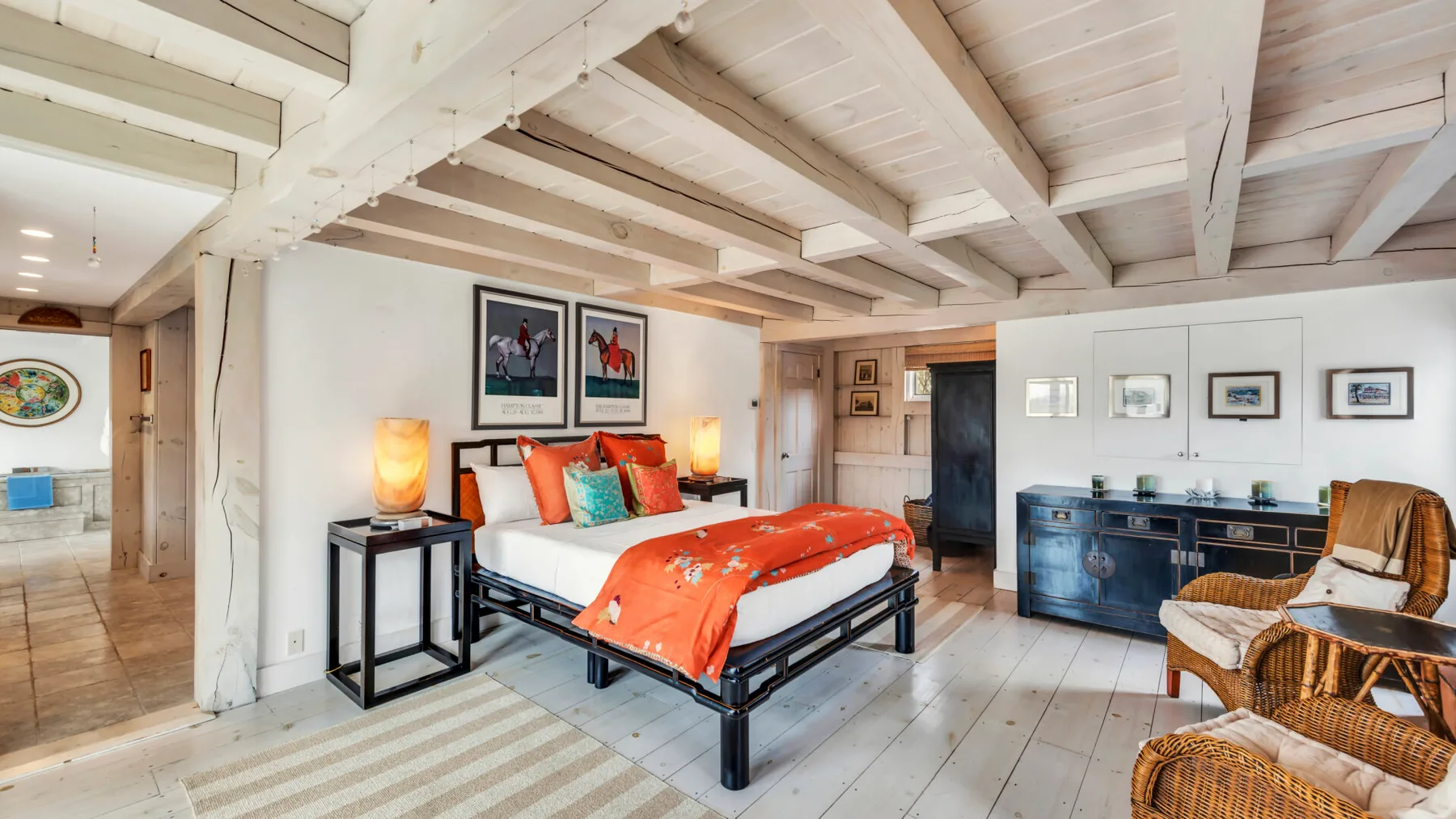 A bedroom with a bed dressed in orange bedding and wicker seating.