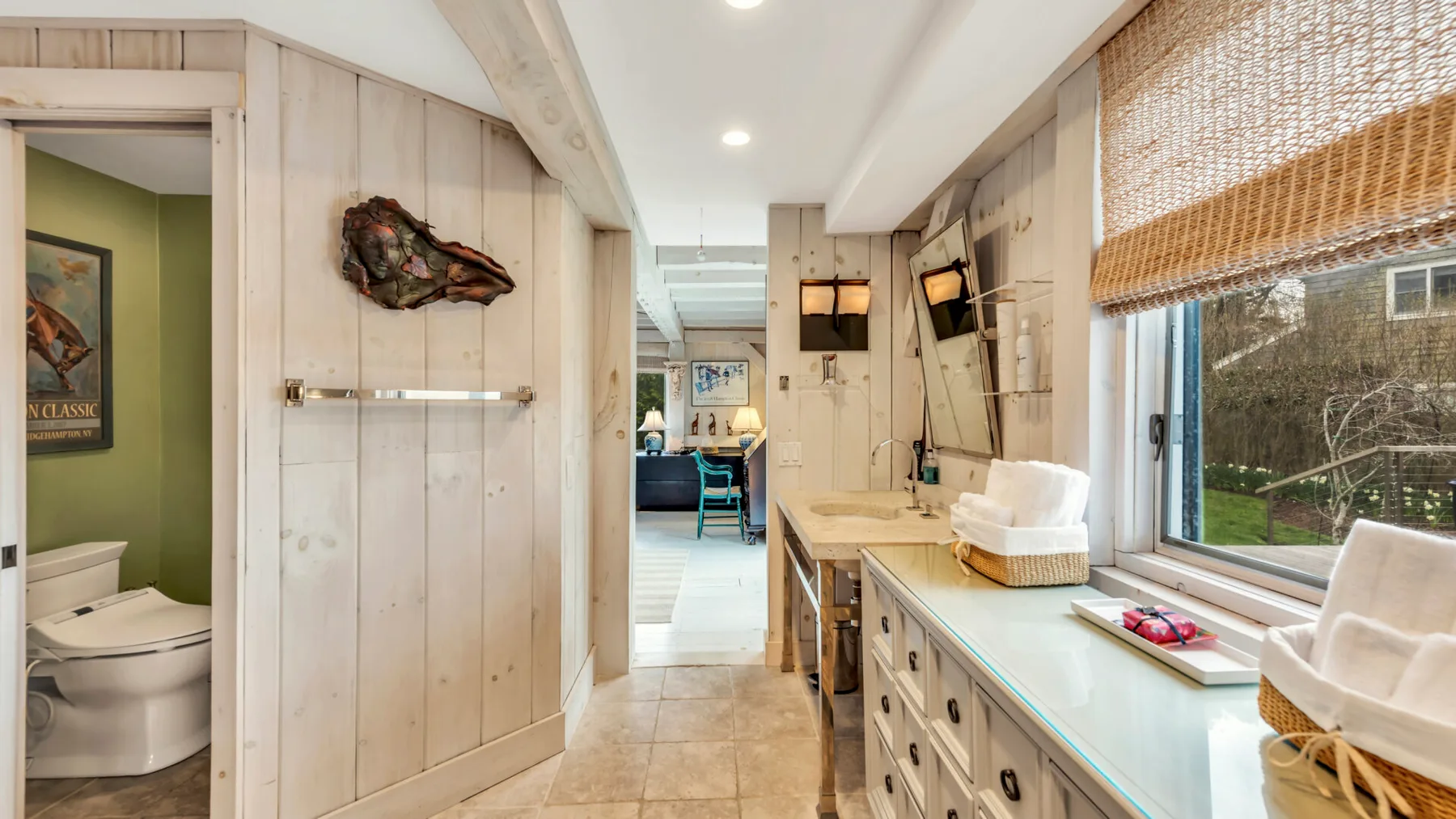 A bright bathroom with a long counter and a toilet in a separate alcove.