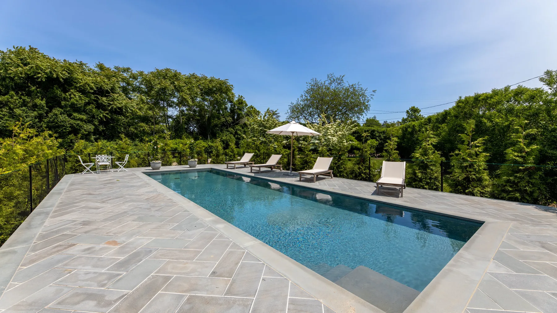 An outdoor swimming pool is surrounded by a paved patio and greenery.