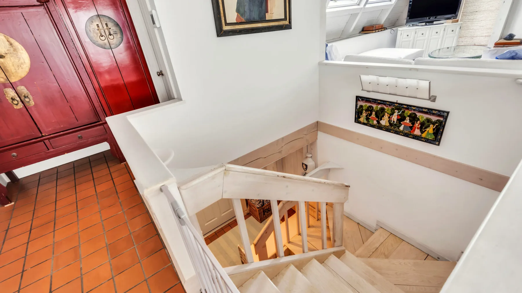A stairwell with white railings descends beside a red cabinet and tiled floor.
