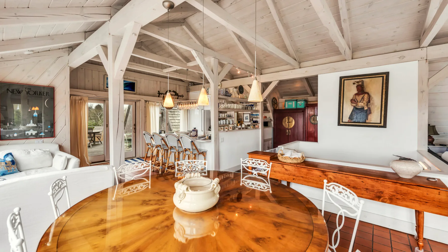 A rustic dining area with a long wooden table and white chairs beneath exposed beams.