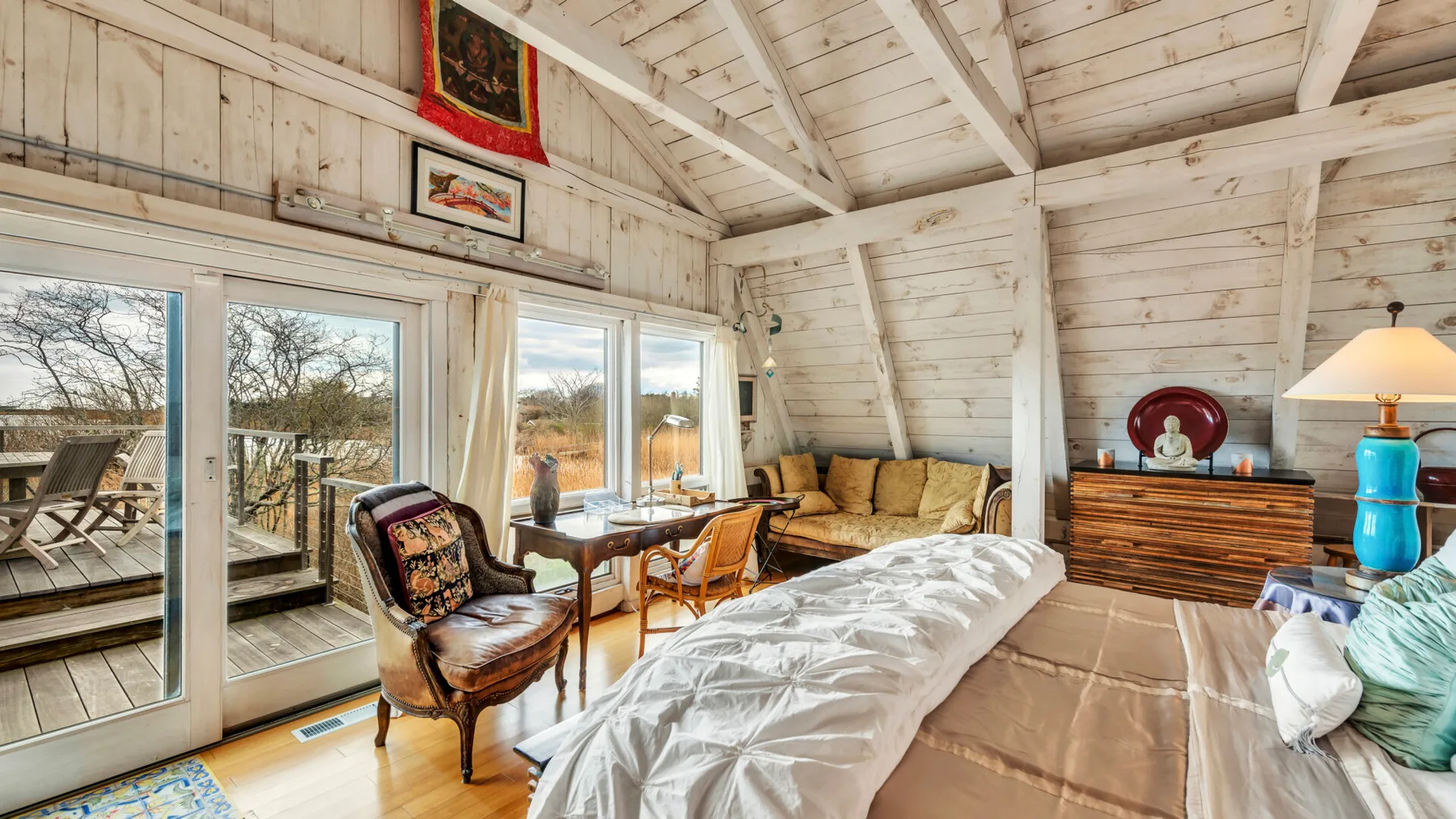 A bedroom with a bed, seating, and large windows overlooking a deck.