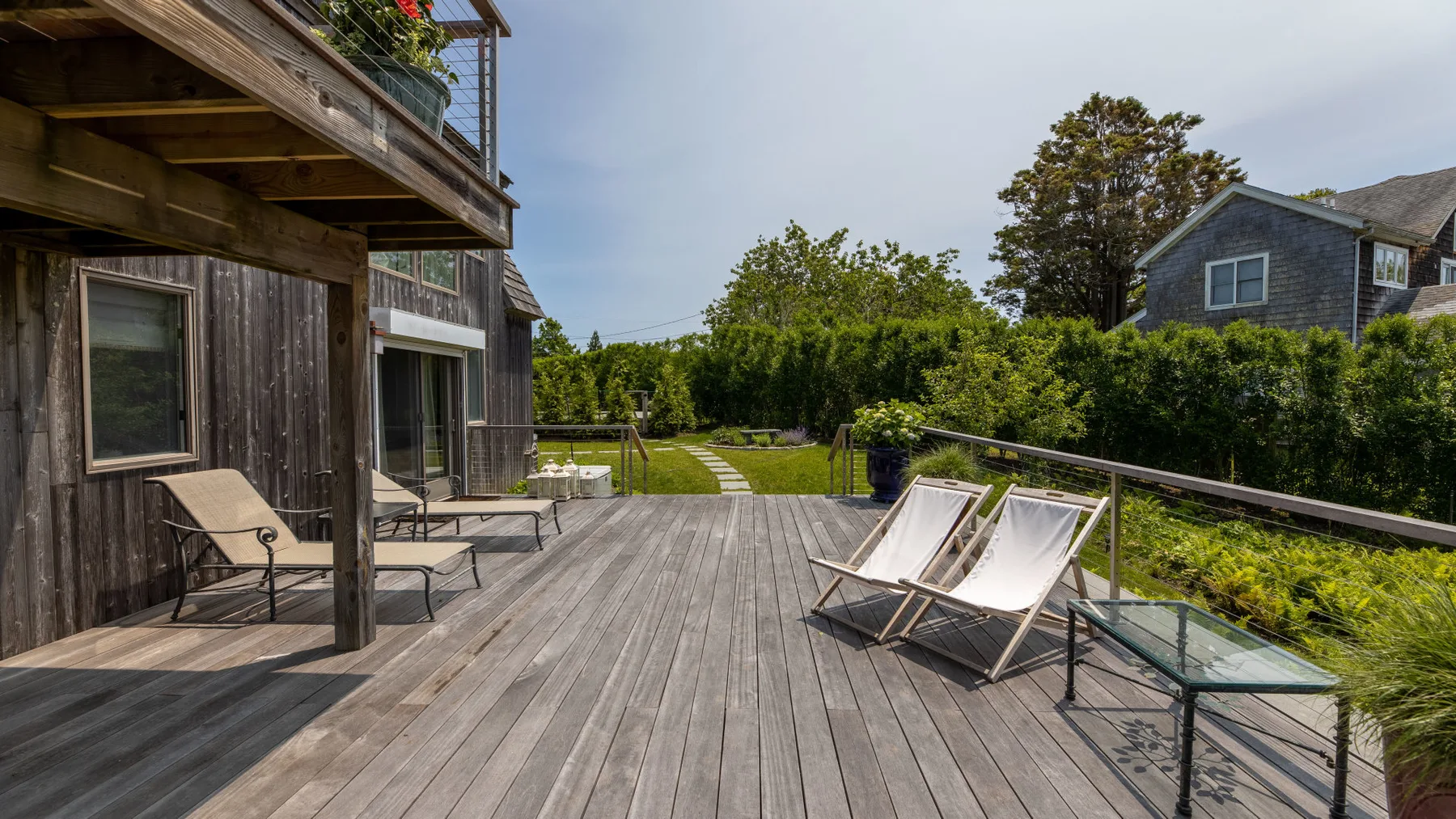 A spacious wooden deck with outdoor seating overlooks a green yard.
