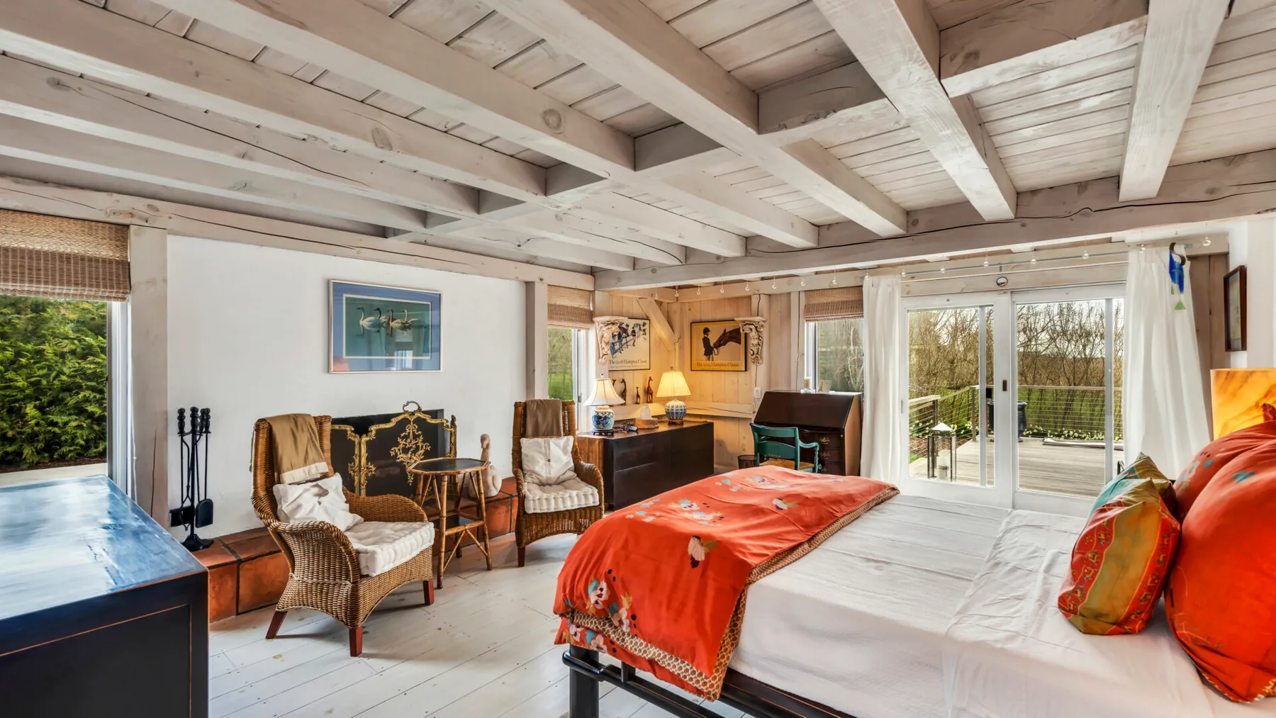 A bedroom with a bed covered by an orange blanket and doors opening onto a patio.