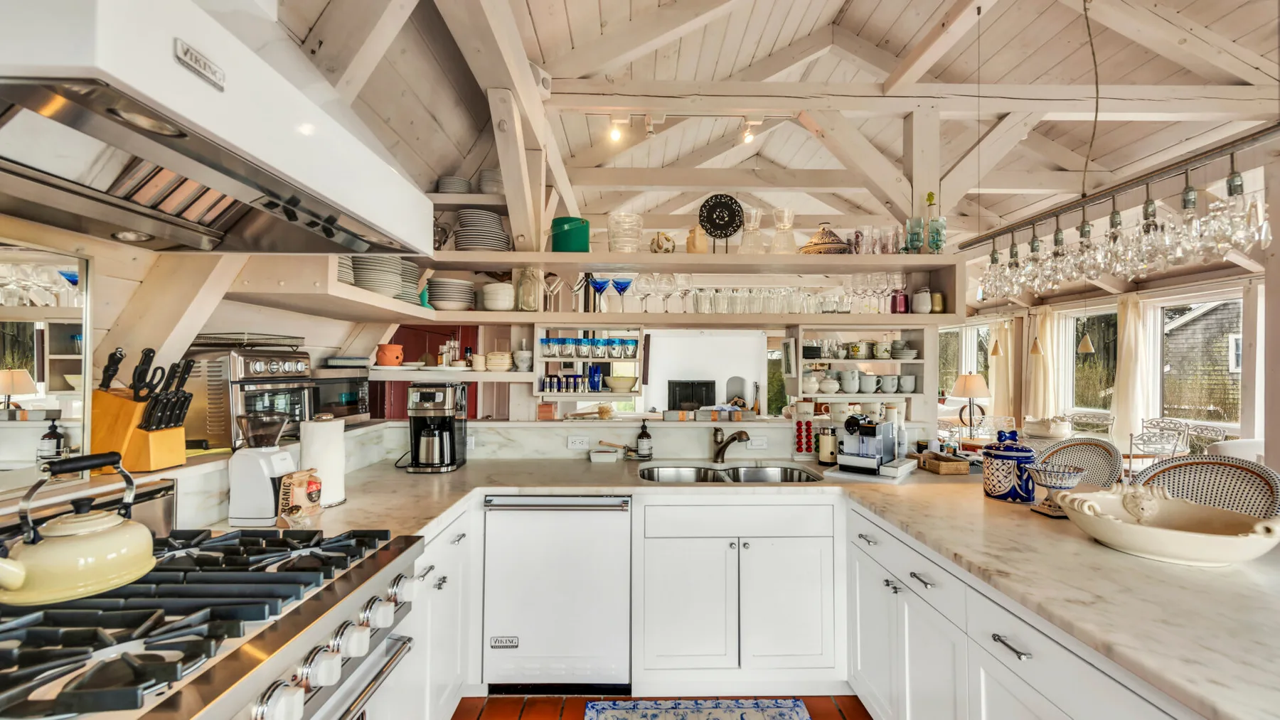 A bright kitchen with white cabinetry, a central counter, and exposed ceiling beams.