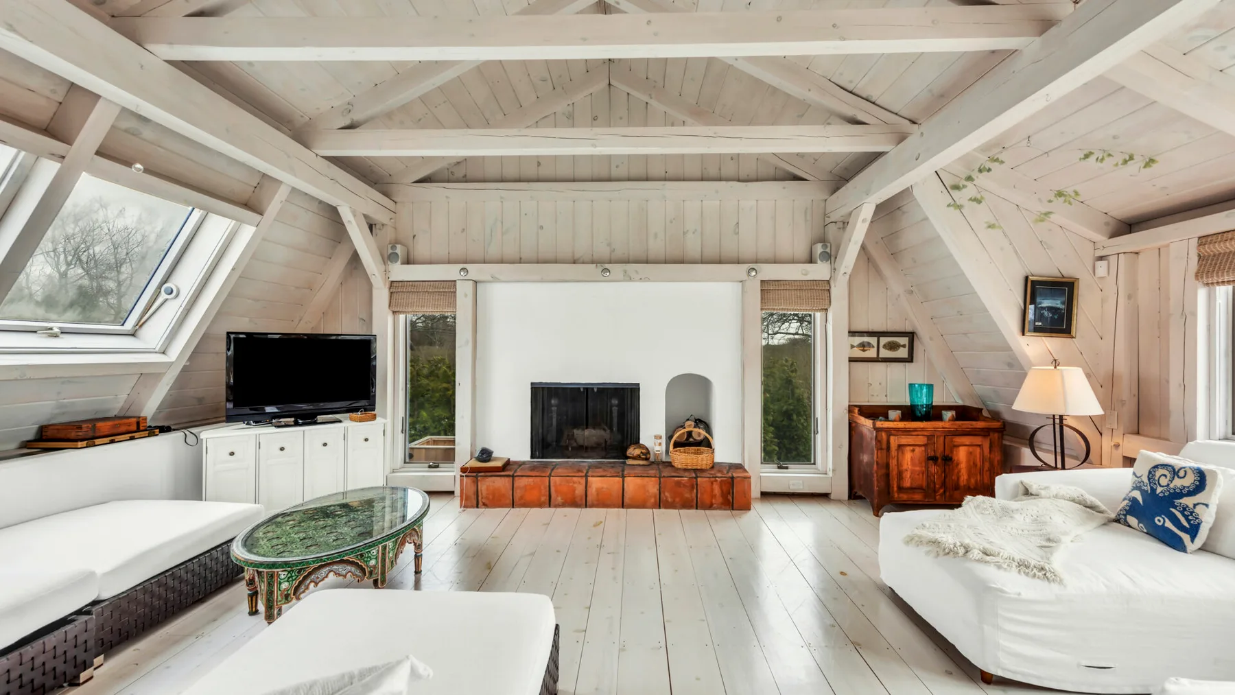 A bright living room with white seating, a fireplace, and exposed wooden beams.