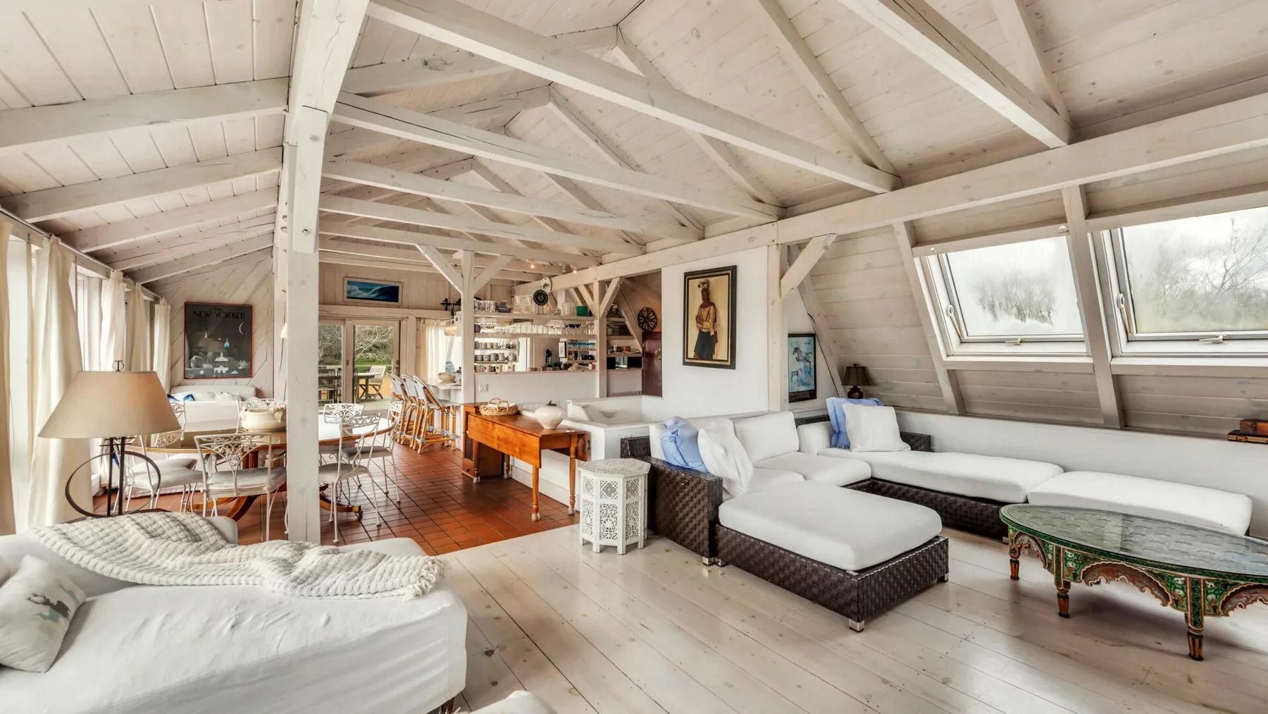A bright open-plan living and dining area with exposed white beams and seating.