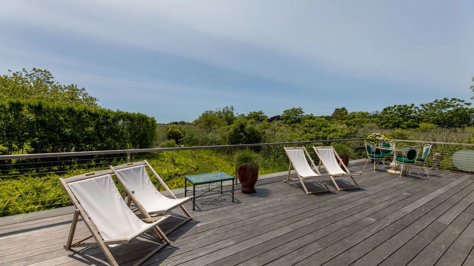 An outdoor deck has reclining seating, a small table, and views of green vegetation.