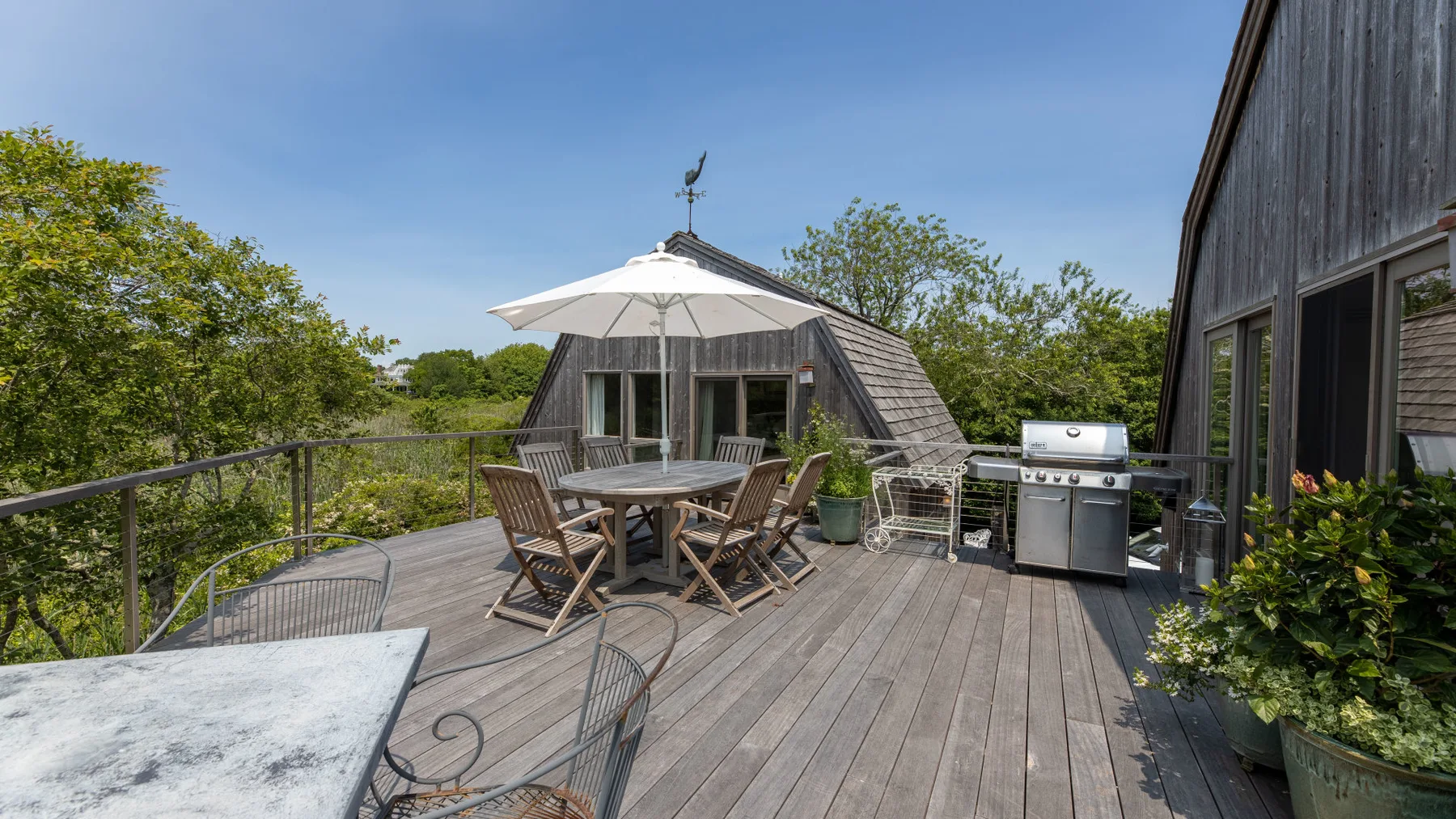 A wooden deck with outdoor seating, a large umbrella, and a grill.