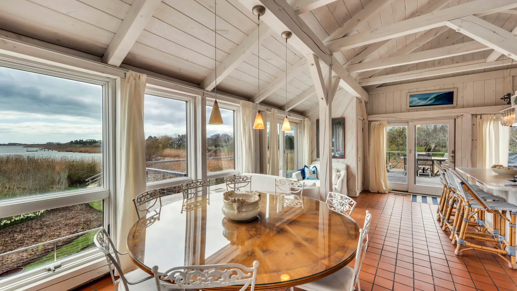 A bright dining room with a long table, large windows, and exposed ceiling beams.
