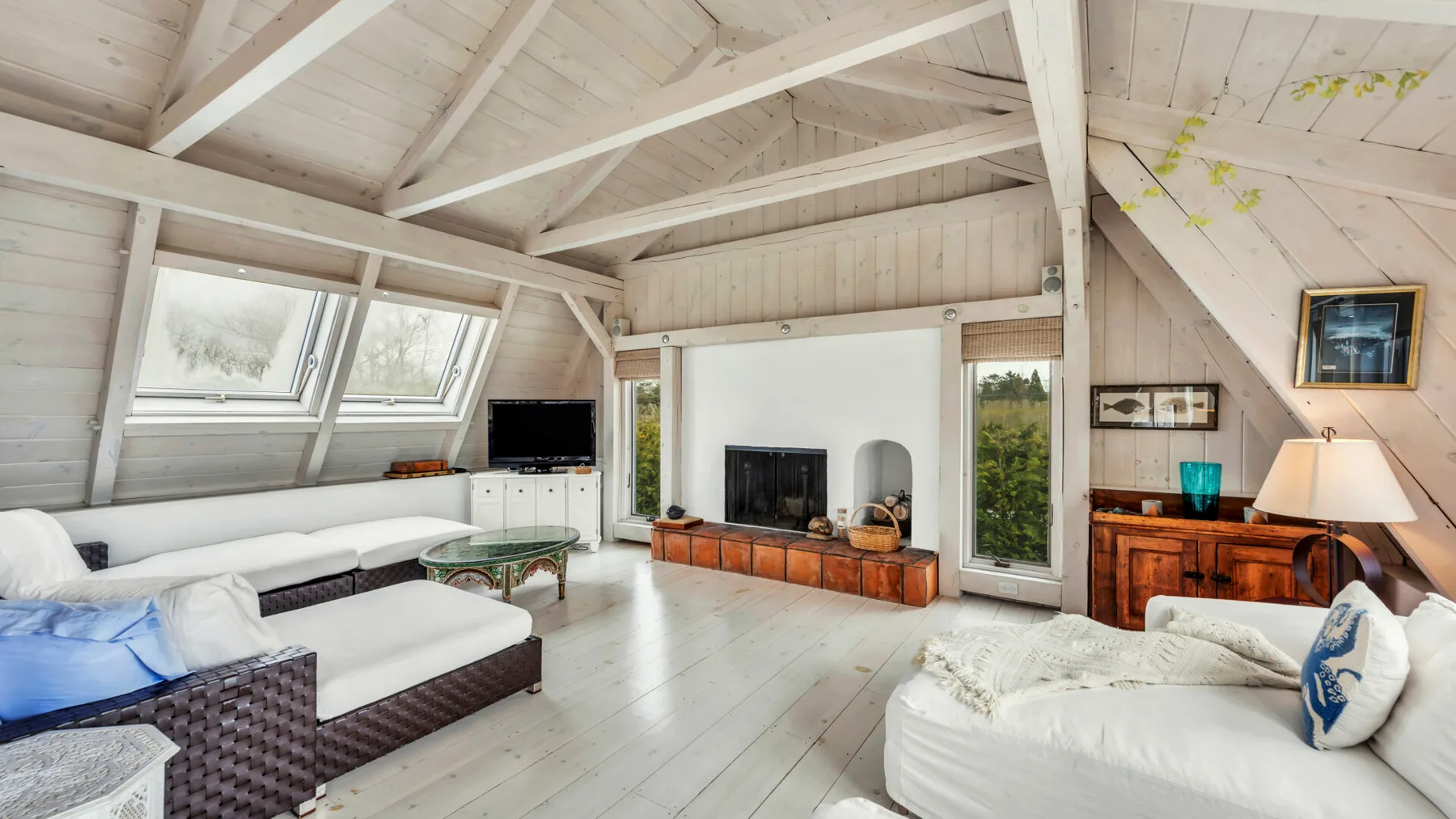 A bright living room with a fireplace, seating, and large sloped windows.