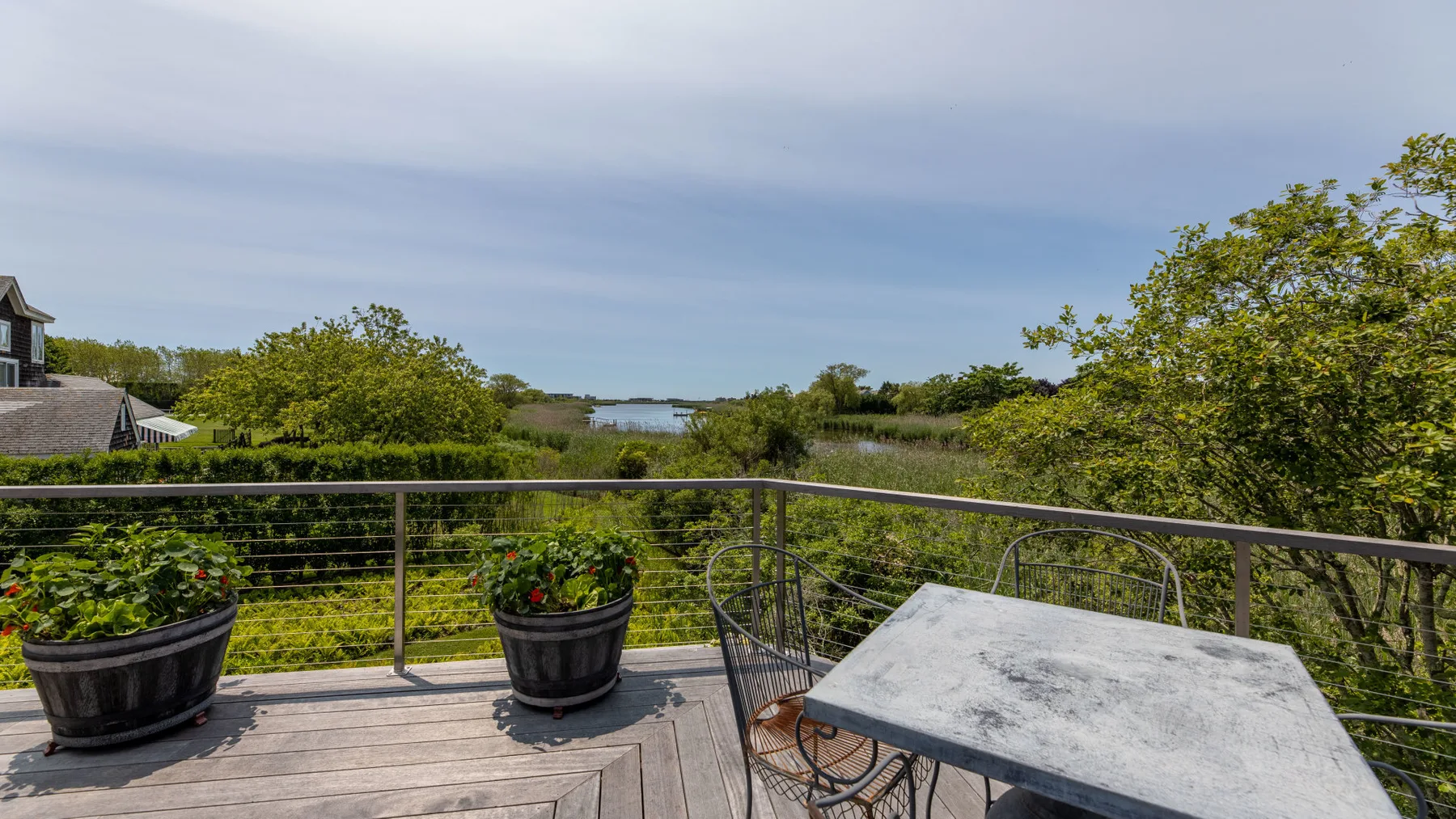 A balcony with a table and potted plants overlooks a green landscape.