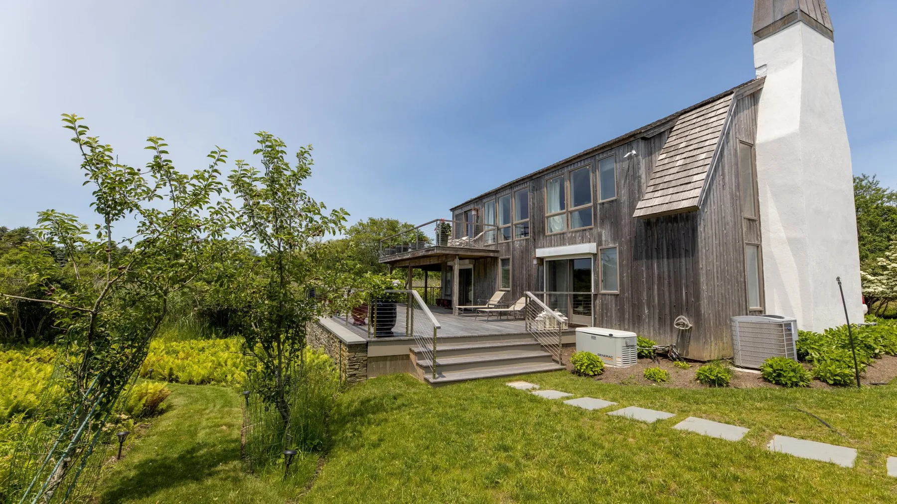 A modern house with a broad wooden deck and surrounding greenery.