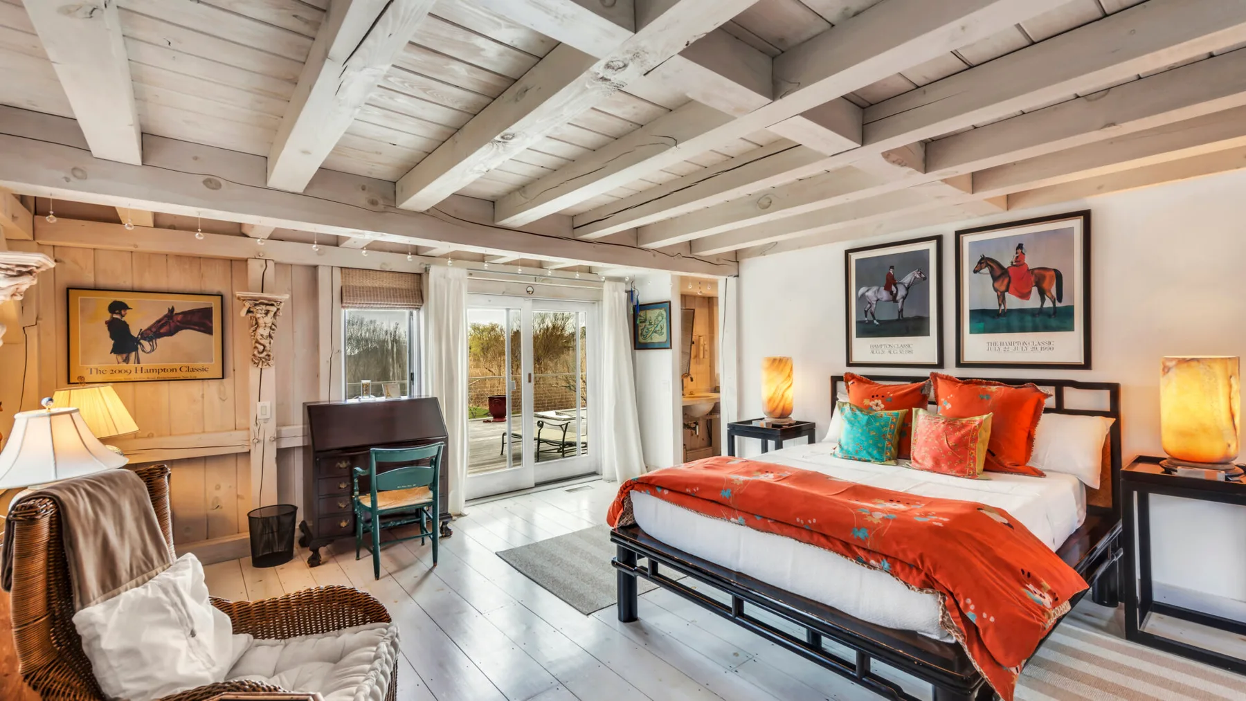 A bedroom with a red-covered bed, a desk, and glass doors opening to a patio.
