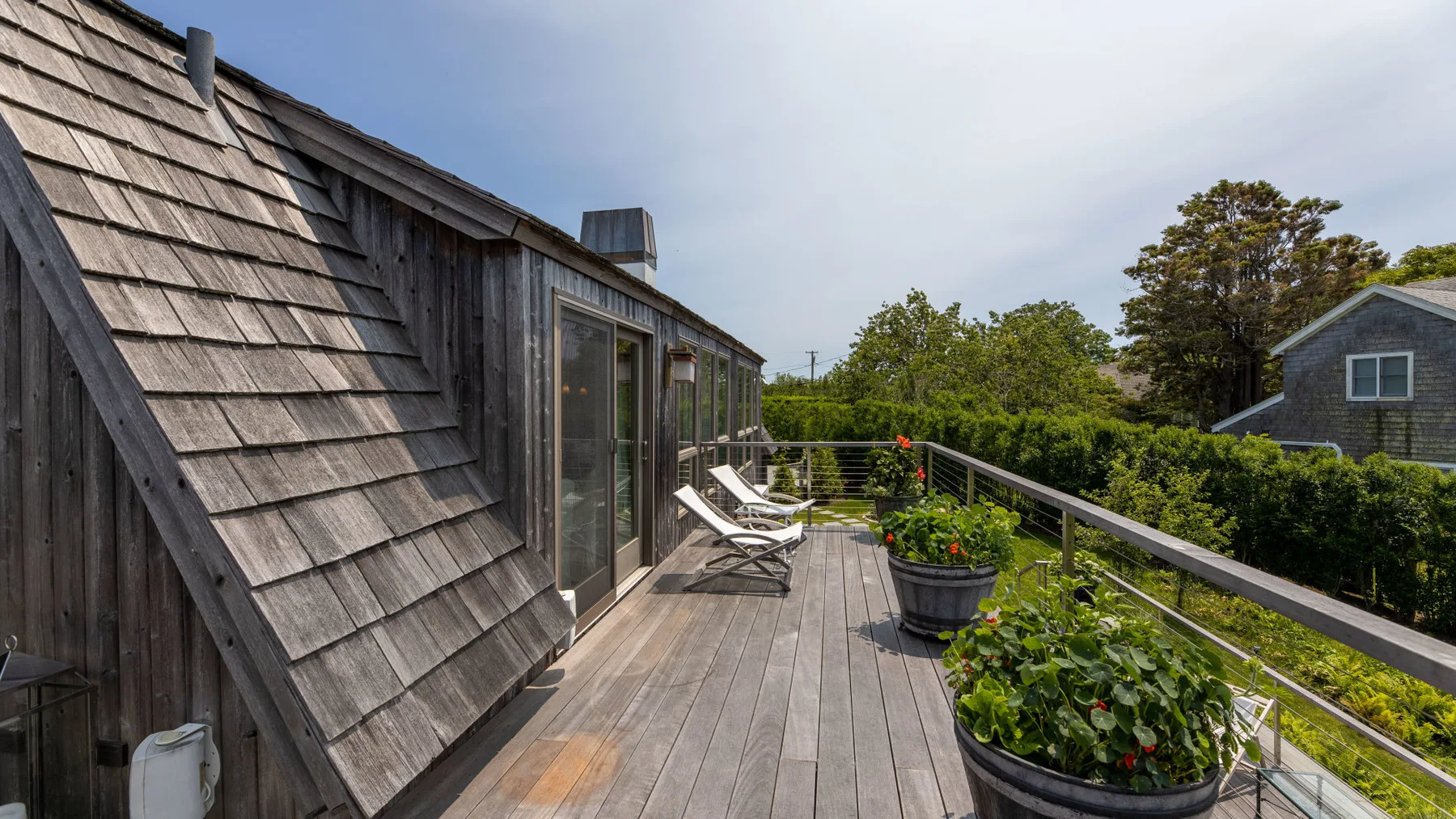 A wooden rooftop deck has lounge seating and planters beside a railing.