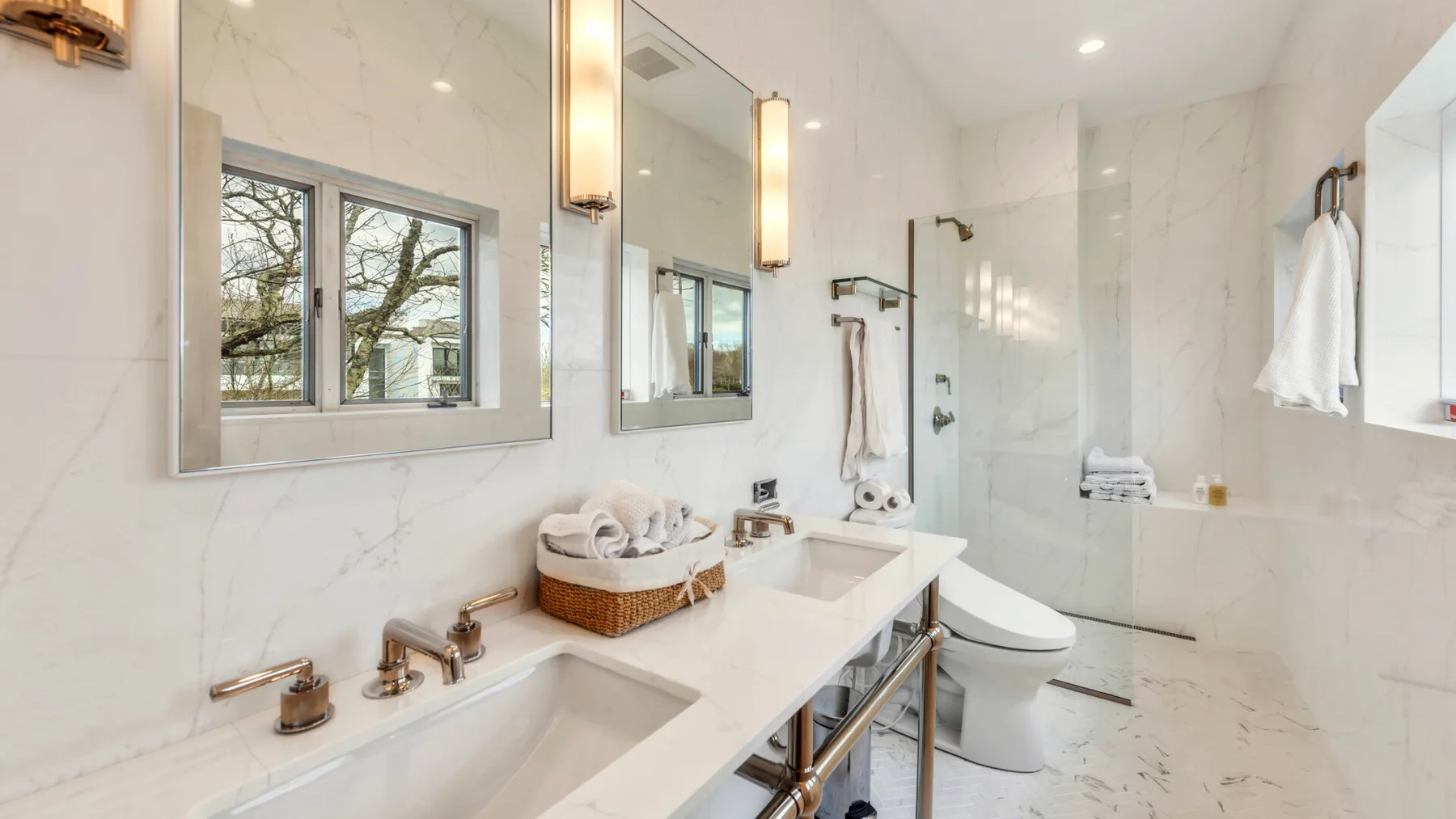 A bright bathroom with a double vanity, toilet, and glass shower.