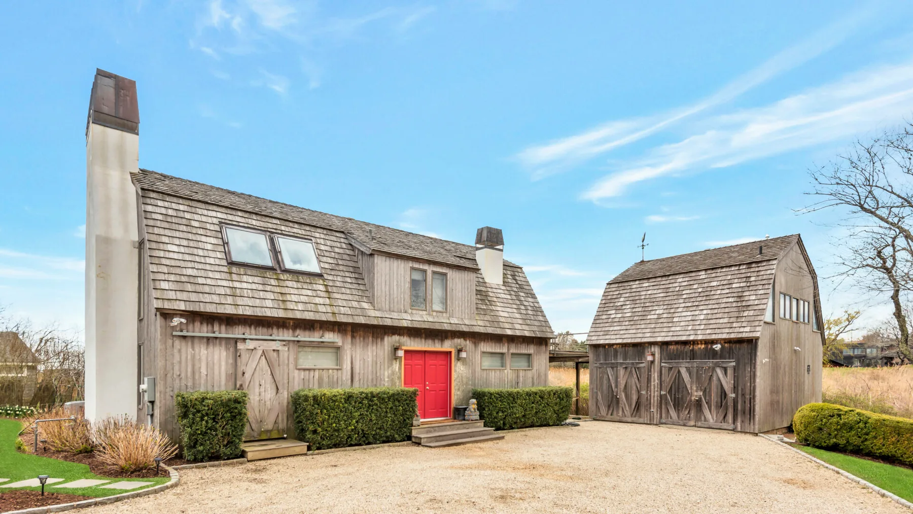 A rustic barn-style building with a red door stands beside a wooden outbuilding.