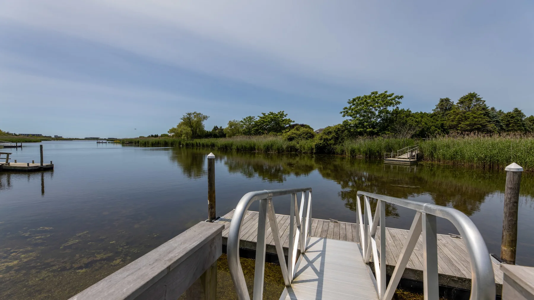 A small dock extends over calm water, with trees and reeds along the far bank.