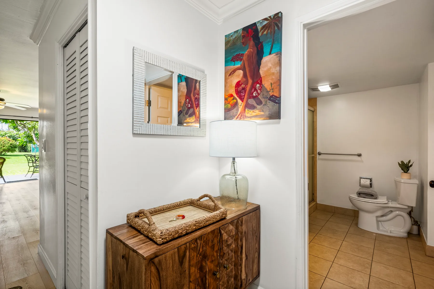 A bright hallway has a wooden console and lamp beside an open bathroom.