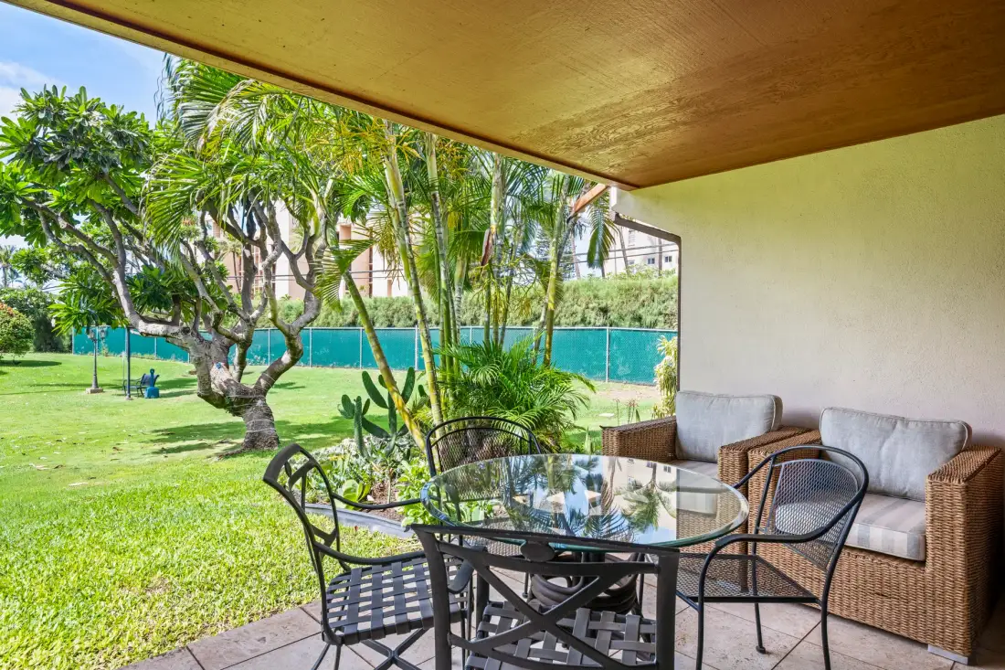 A covered outdoor seating area with a glass table overlooks a green lawn.