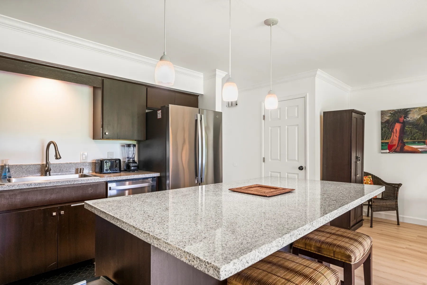 A kitchen with a large island, dark cabinets, and stainless steel appliances.