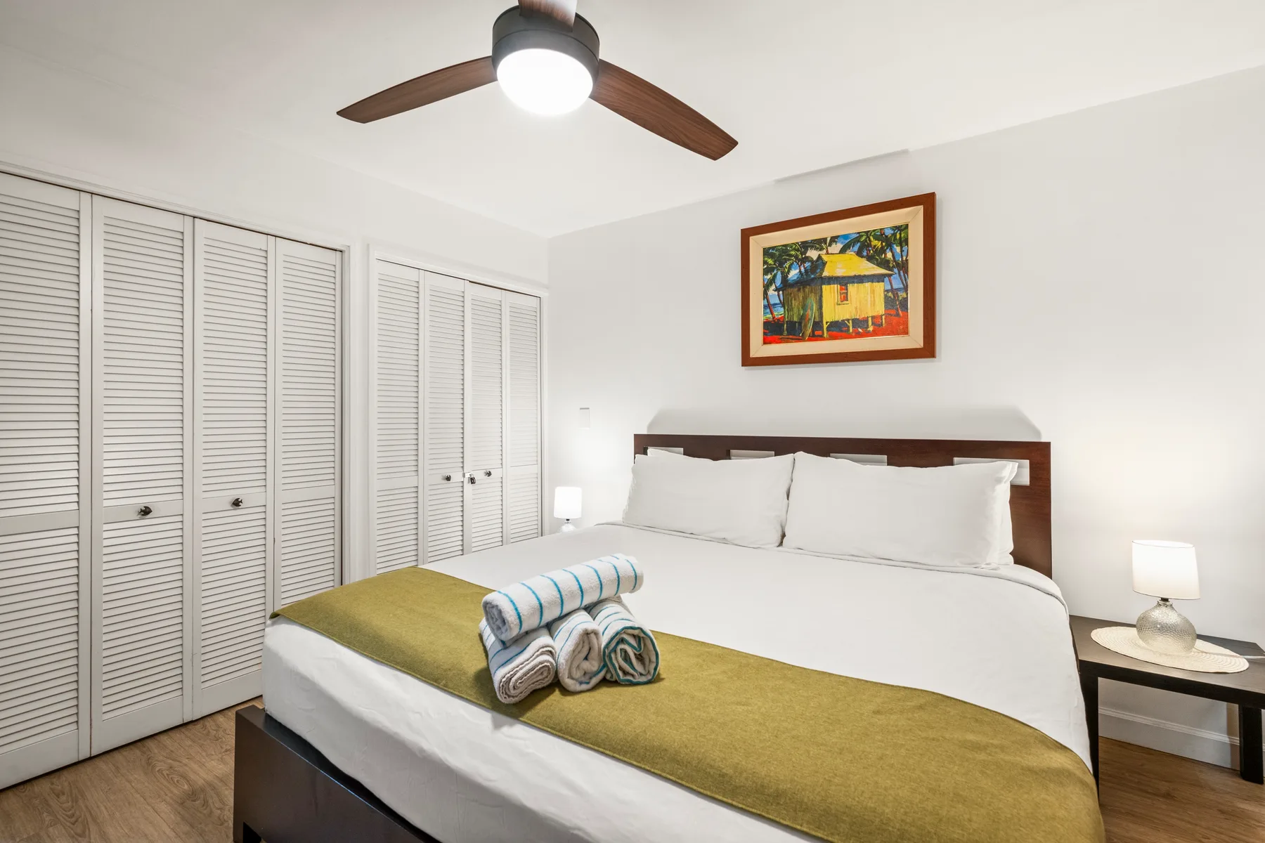 A bedroom with a large bed and white louvered closet doors.