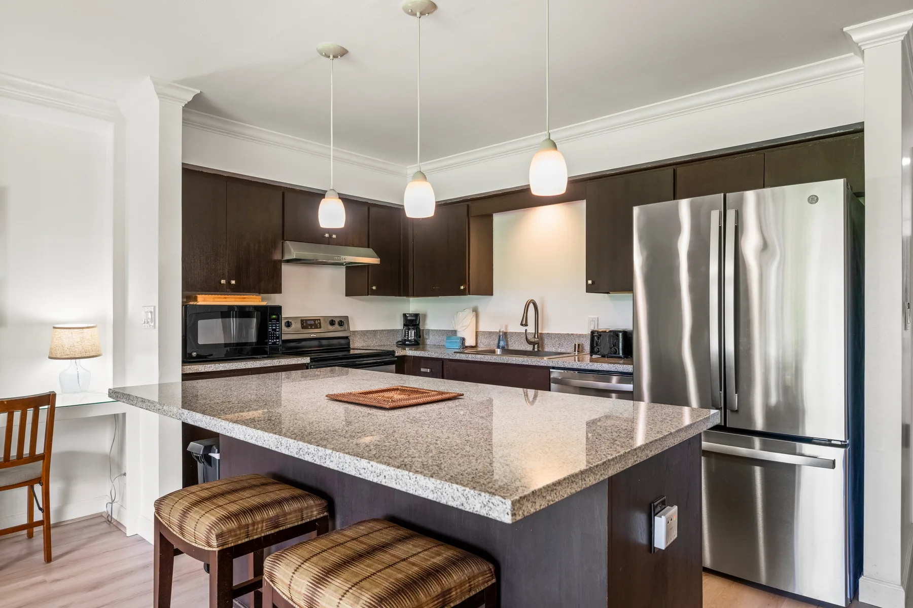 A modern kitchen with a large island, dark cabinets, and stainless steel appliances.